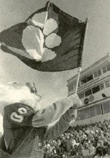 博比在一场足球比赛中挥舞着熊猫旗.  鲍比在他那件经典的00号球衣外面穿了一件工装裤.